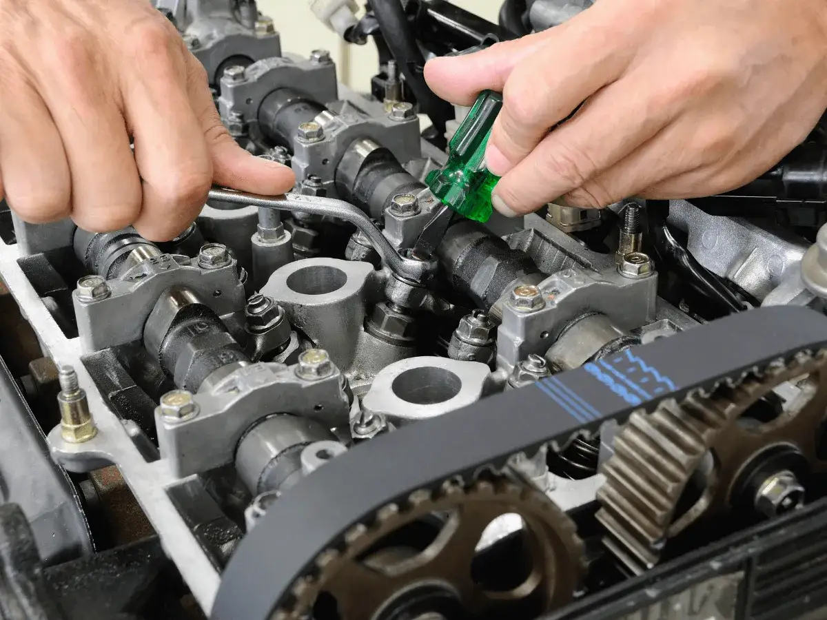 Mechanik dokonuje precyzyjnej regulacji zaworów silnika, używając klucza i małego śrubokręta.