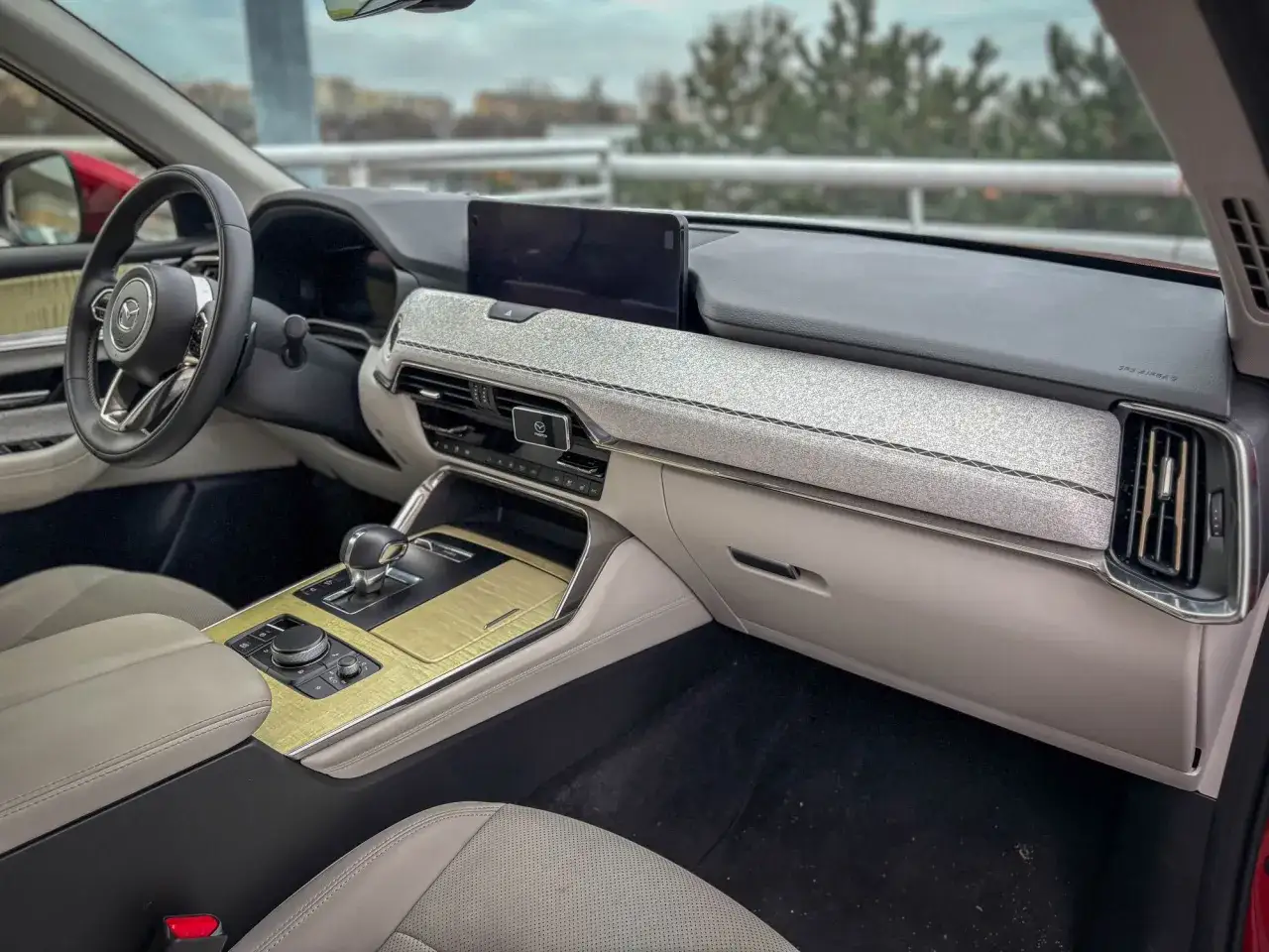 Wnętrze Mazdy CX-60 3.3 diesel z jasną tapicerką, drewnianymi wstawkami i ekranem multimedialnym.
