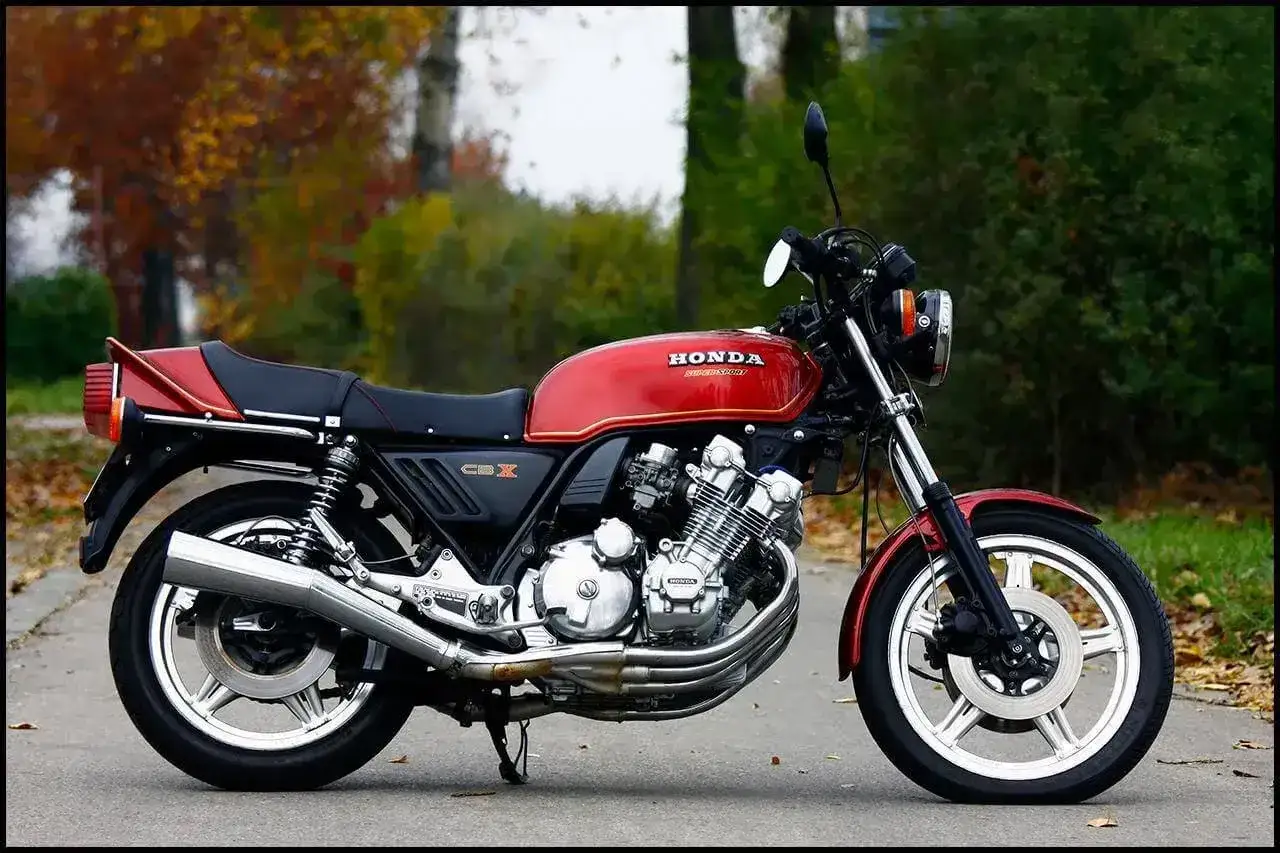 Klasyczny czerwony motocykl Honda CBX 1000 z lat 80. stoi na drodze, otoczony jesienną zielenią i opadłymi liśćmi.
