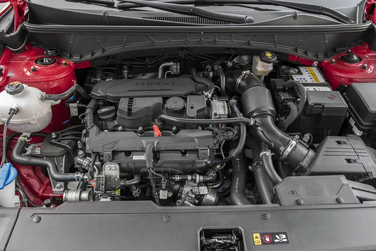Silnik Hyundai Tucson 1.6 T-GDI z turbodoładowaniem. Widoczne elementy układu dolotowego, akumulator i płyny eksploatacyjne.
