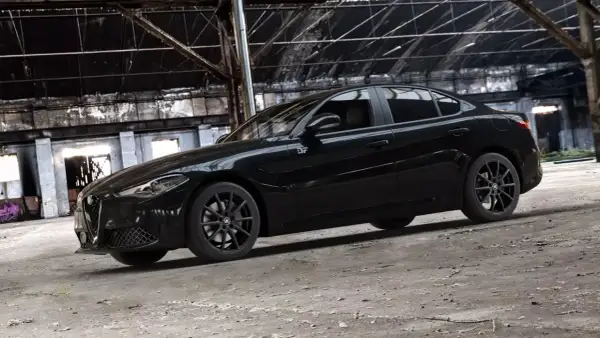 Czarny Alfa Romeo Giulia Quadrifoglio w opuszczonej hali przemysłowej.