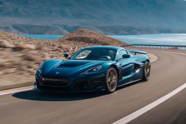 Niebieski Rimac Nevera sunie po krętej drodze nad turkusowym morzem, otoczony skalistym krajobrazem.