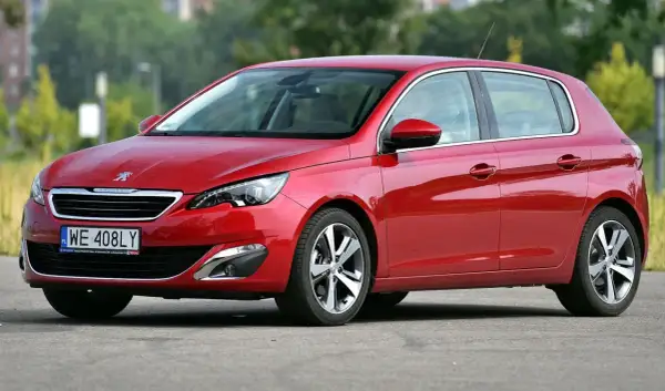 Czerwony Peugeot 308 T9 na tle zieleni, z widocznym numerem rejestracyjnym WE 408LY.