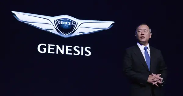 Mężczyzna w garniturze stoi obok logo Genesis, marki luksusowych samochodów.
