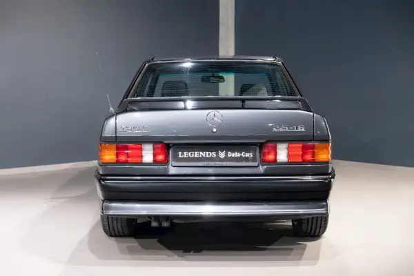 Tył szarego Mercedesa 190 2.5-16 z lat 80. z antenką i emblematami.