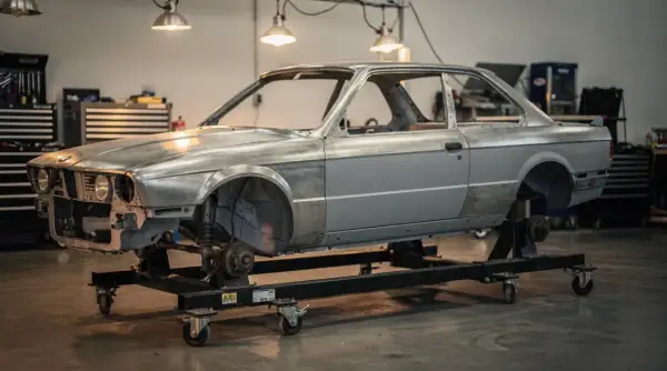 Karcass BMW E30 na wózku warsztatowym, gotowy do renowacji. Marzenie o **prawie jazdy a2** i własnym aucie zaczyna się od takich projektów.