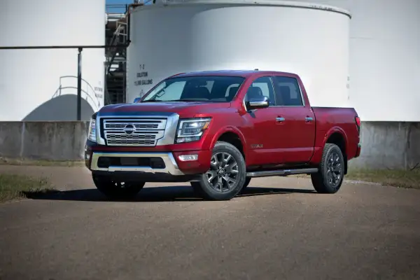 Czerwony Nissan Titan stoi przed dużymi białymi zbiornikami.