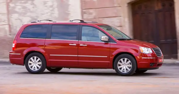 Czerwony Chrysler Grand Voyager w ruchu, z przyciemnianymi szybami i relingami dachowymi, przemierza ulicę.