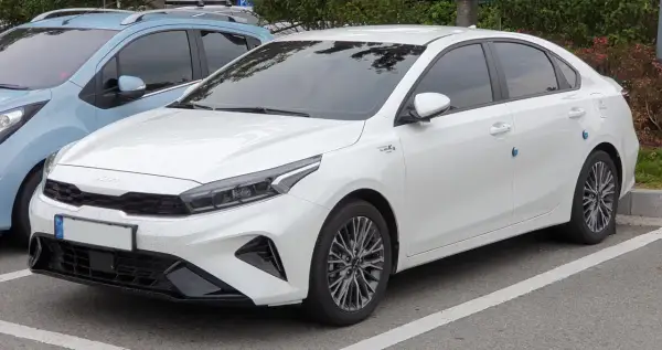 Biały sedan Kia Forte zaparkowany na parkingu, widok z przodu i z boku.