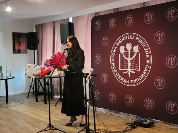 Kobieta przemawia na tle baneru z logo biblioteki, podczas wydarzenia w Garwolinie. Wgm rejestracja.