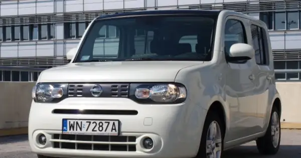 Biały Nissan Cube z polskimi tablicami rejestracyjnymi WN 7287A zaparkowany przed nowoczesnym budynkiem.