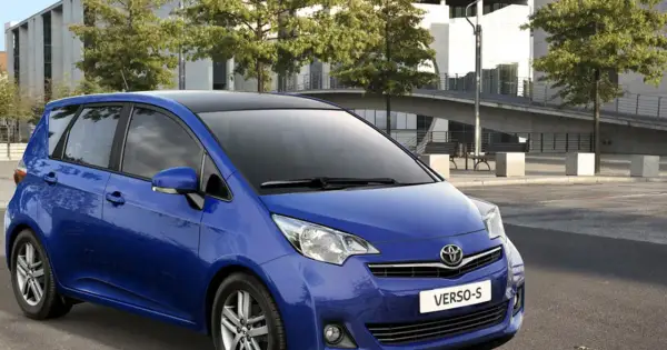 Niebieski Toyota Verso S z czarnym dachem zaparkowany przed nowoczesnym budynkiem.