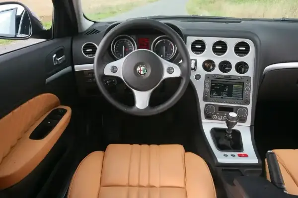 Wnętrze Alfa Romeo 159 1.9 JTD z brązową skórzaną tapicerką, kierownicą i panelem środkowym.