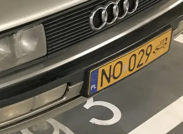 Zbliżenie na przód samochodu Audi z charakterystycznym grillem i logo. Widoczne żółte tablice rejestracyjne z numerem NO 029.