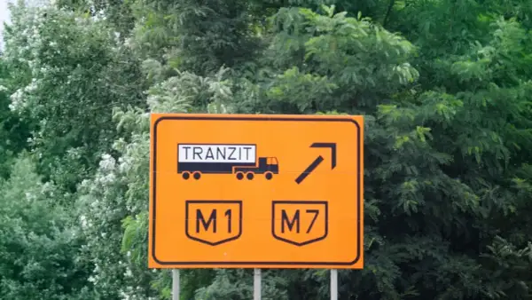 Pomarańczowy znak drogowy w drodze na Węgry. Informuje o tranzycie ciężarówek na autostrady M1 i M7.