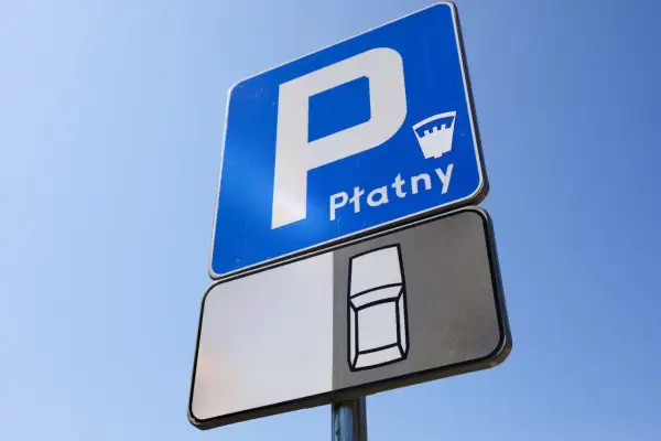 Znak D18 informuje o płatnym parkingu. Widoczny jest symbol samochodu na tablicy pod znakiem.