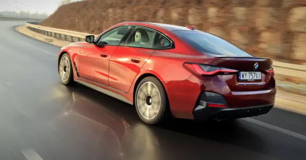 Czerwone BMW 4 Gran Coupé pędzi po zakręcie drogi, odbijając się w mokrej nawierzchni.