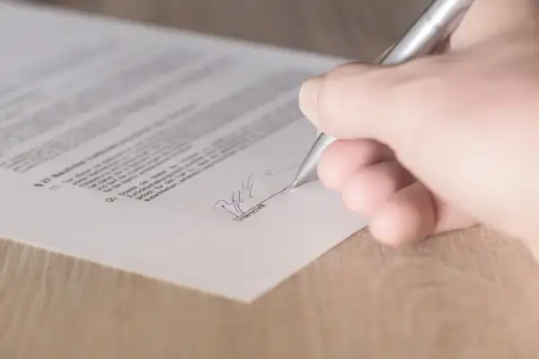 Dłoń podpisuje dokument, być może kartę pojazdu.