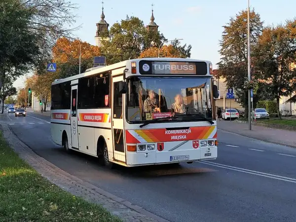 Autobus komunikacji miejskiej z napisem "TURBUSS" na tablicy kierunku, na ulicy w jesienny dzień. Rejestracja ELU.