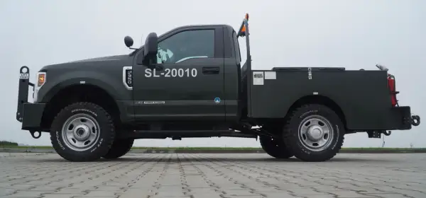 Ciemnozielony Ford F350 z platformą, numerem SL-20010 i pomarańczowym kogutem na dachu.