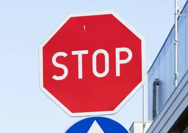 Czerwony znak stop z białym napisem "STOP" na tle błękitnego nieba i nowoczesnego budynku.