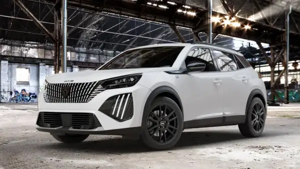 Biały Peugeot 2008 GT z czarnymi felgami stoi w opuszczonej hali przemysłowej, gdzie światło przebija się przez dach.