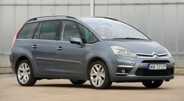 Szary Citroen C4 Grand Picasso 2.0 HDI z kierowcą za kierownicą, zaparkowany przed budynkiem.