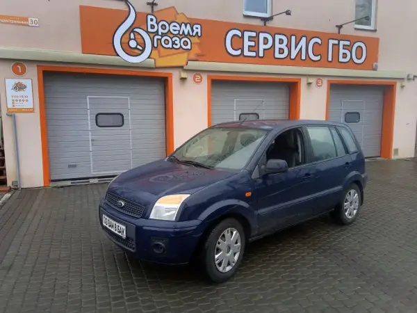 Ciemnoniebieski Ford Fusion 1.4 benzyna przed budynkiem serwisu gazowego.