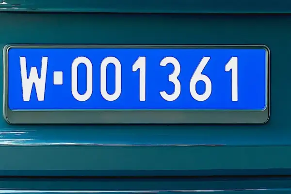 Niebieskie tablice rejestracyjne z numerem W-001361 na ciemnozielonym samochodzie.