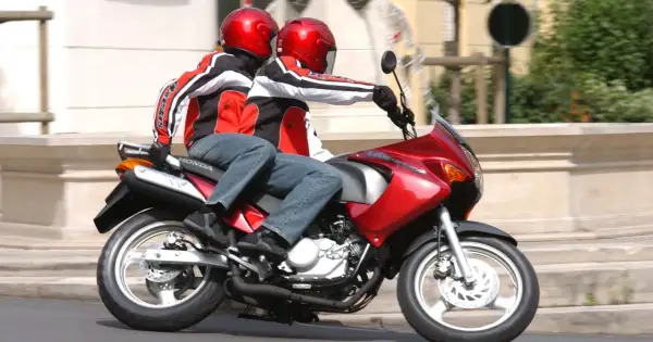 Dwie osoby w czerwonych kaskach i kurtkach jadą na czerwonym motocyklu. To świetna kategoria a1 dla miłośników wolności.