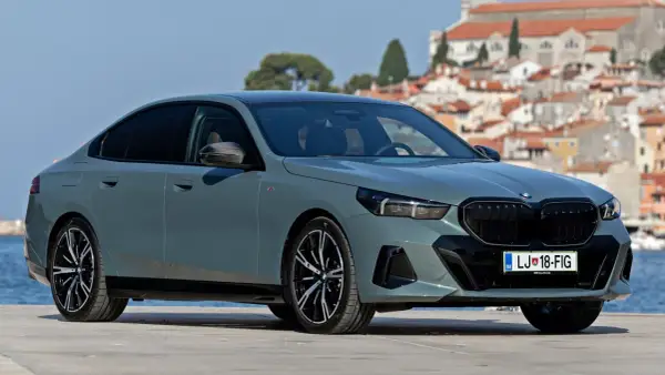 Nowe BMW Serii 5 w kolorze szarym, zaparkowane na tle malowniczego miasta nad morzem.