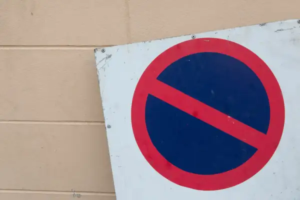 Znak b35 zakazu zatrzymywania się, czerwone koło z niebieskim polem i czerwoną przekątną, przykręcony do jasnej ściany.